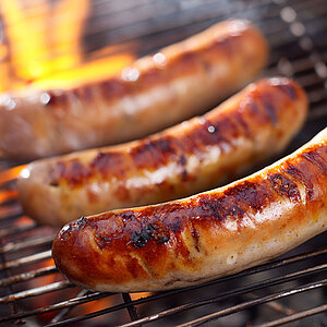 Goldbraun gegrillte Würstchen liegen auf dem Rost über offener Flamme.